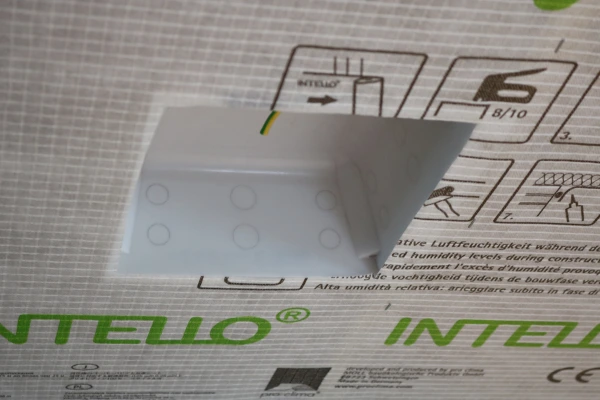 A Fitted Downlight Protector before airtight tape is fixed showing Intello membrane and a cable protruding through the housing.